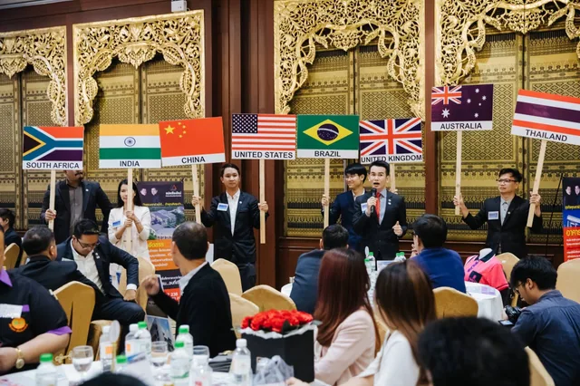Phudit speaking at a business gathering with country placards